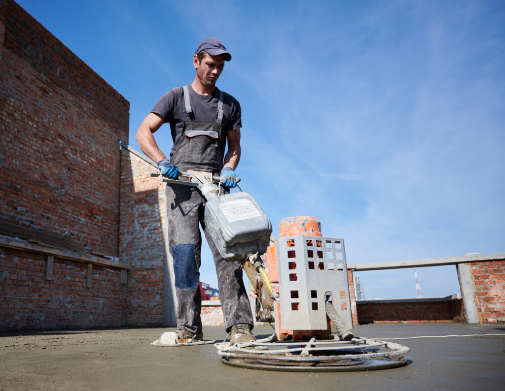 Worker using power trowel machine at construction site.